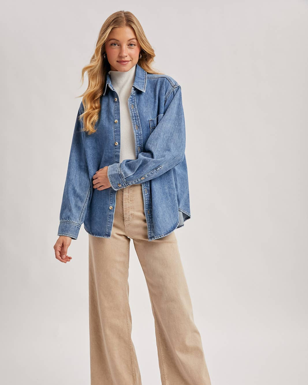 Woman wearing a blue denim jacket, beige pants, and brown boots on a white background