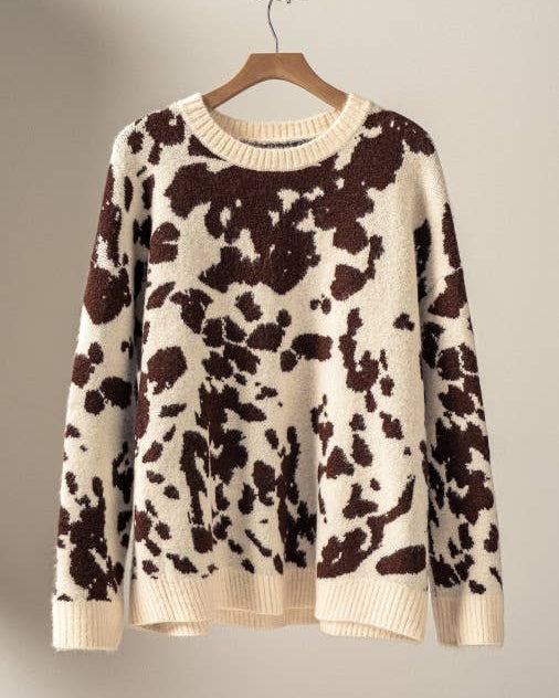 Cow print sweater on a hanger against a plain background