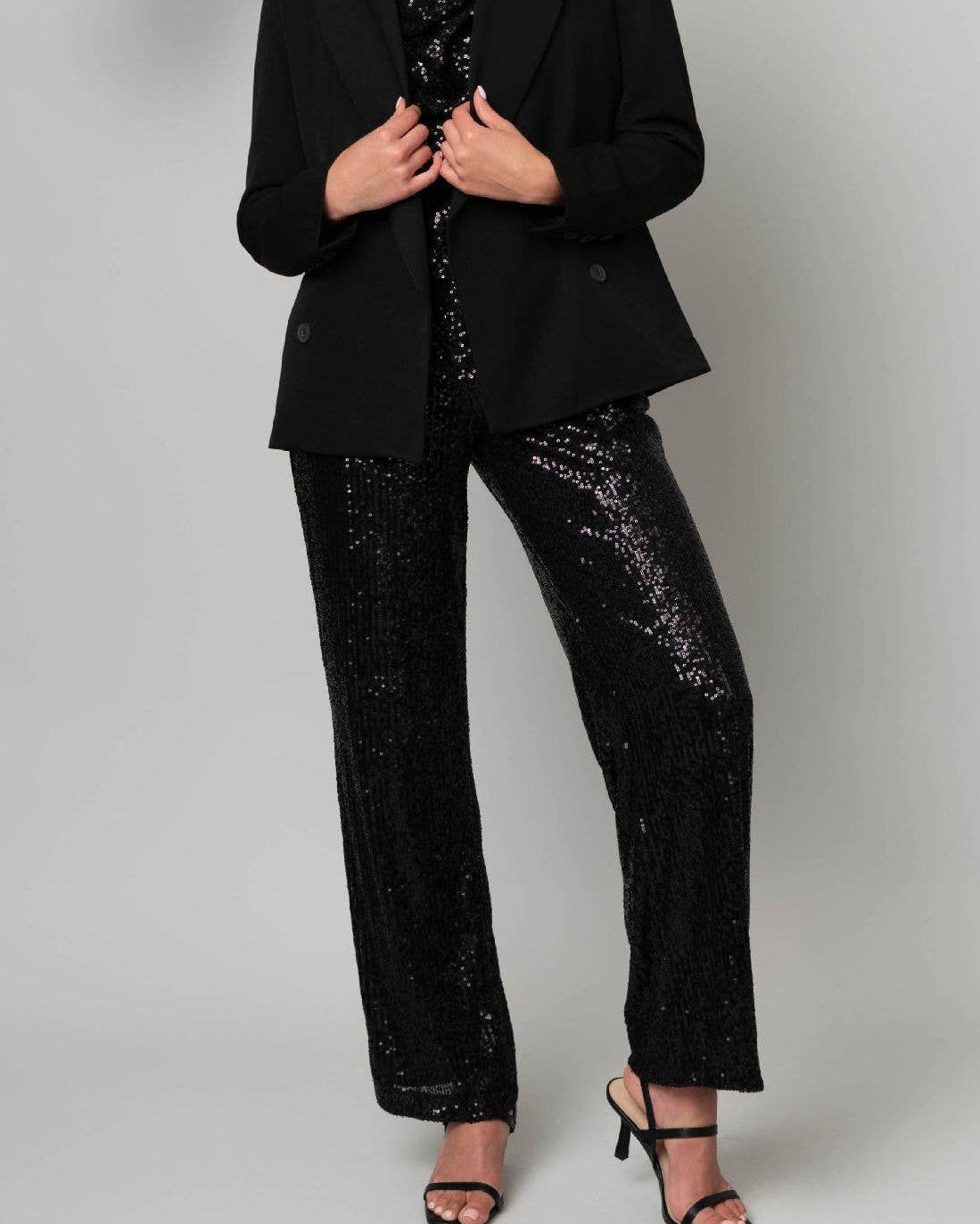 Woman wearing a black suit with sequin pants against a plain background