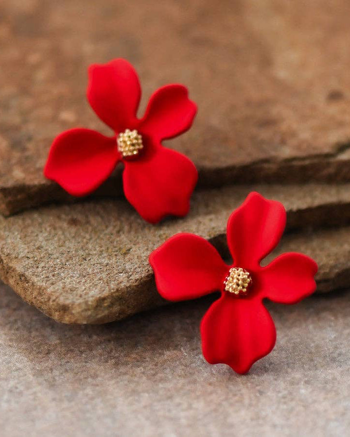 Red flower-shaped earrings with gold centers on a stone surface