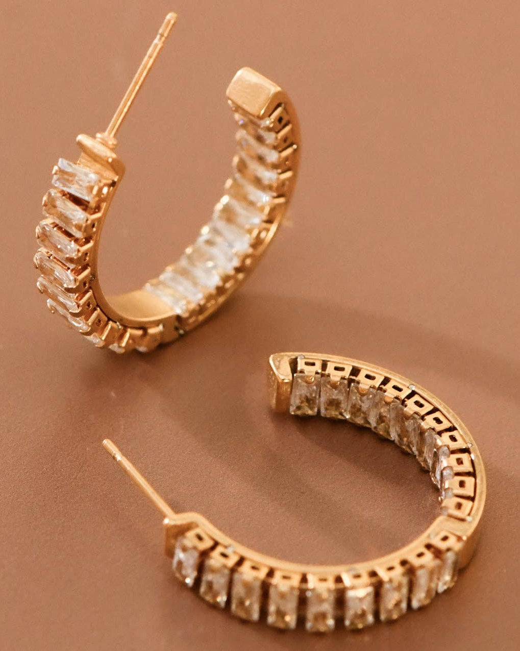Gold hoop earrings with diamond-like stones on a brown background