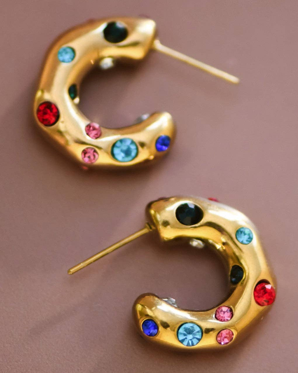 Gold hoop earrings with colorful gemstones on a brown background