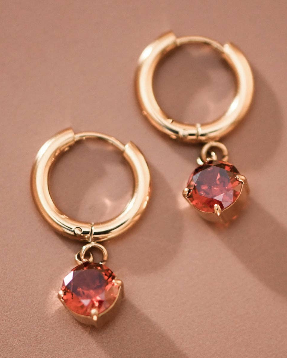 Gold hoop earrings with red gemstones on a brown background