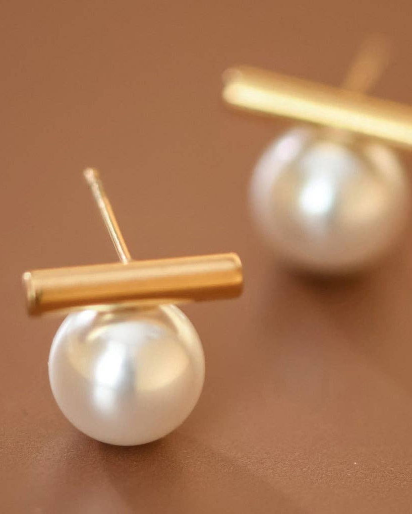 Pearl earrings with gold bars on a brown background