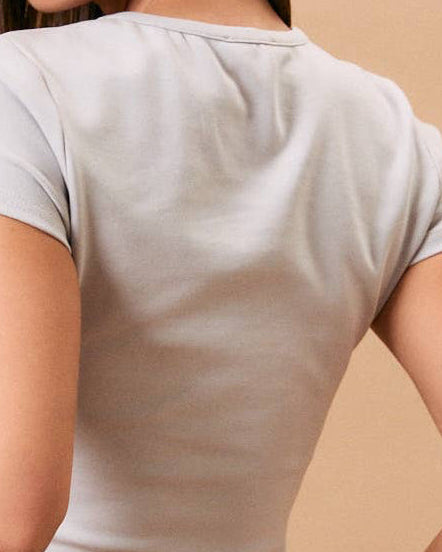 A woman shown from the back wearing a light beige short-sleeve crop top and blue jeans, standing against a solid beige studio background.