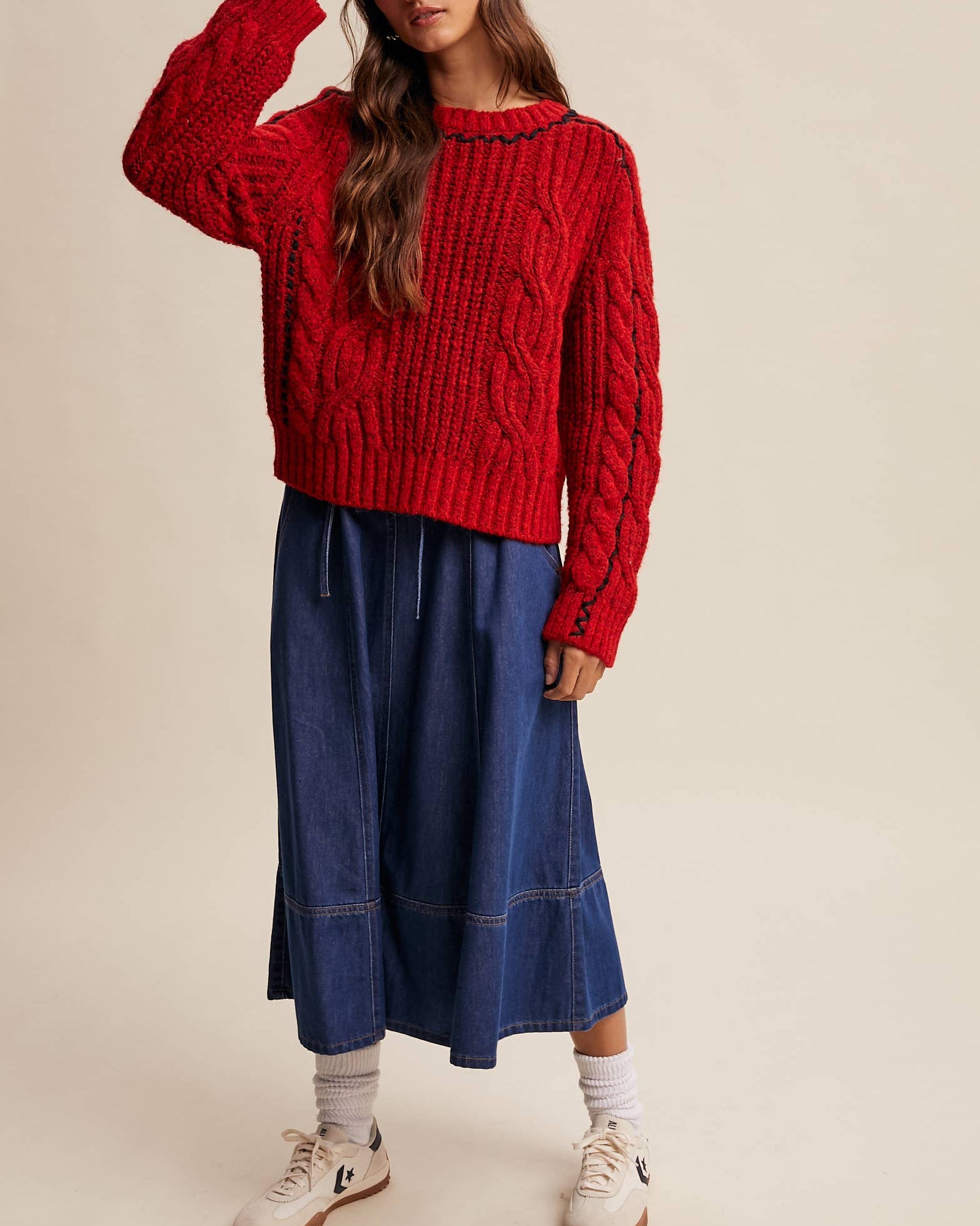 Woman wearing a red sweater and blue skirt against a beige background