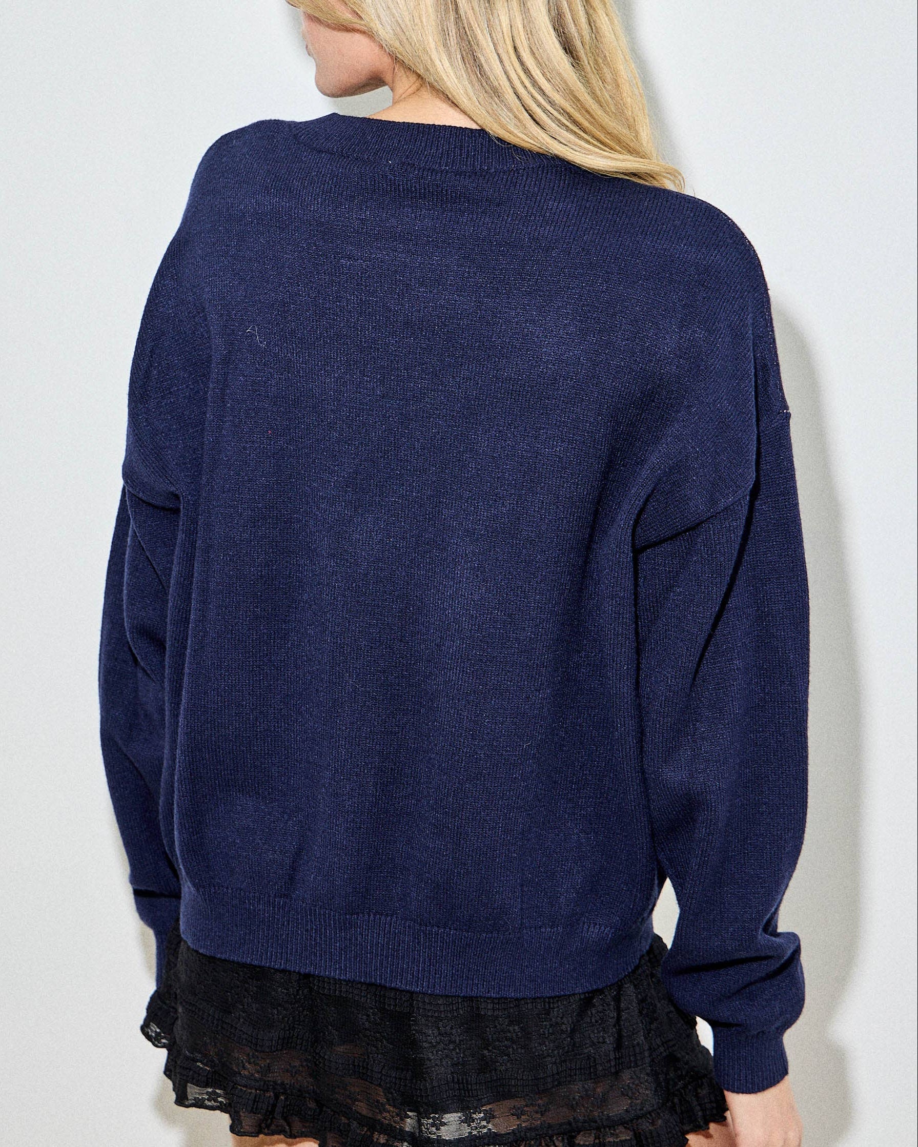 Person wearing a navy blue sweater and black lace skirt against a white background