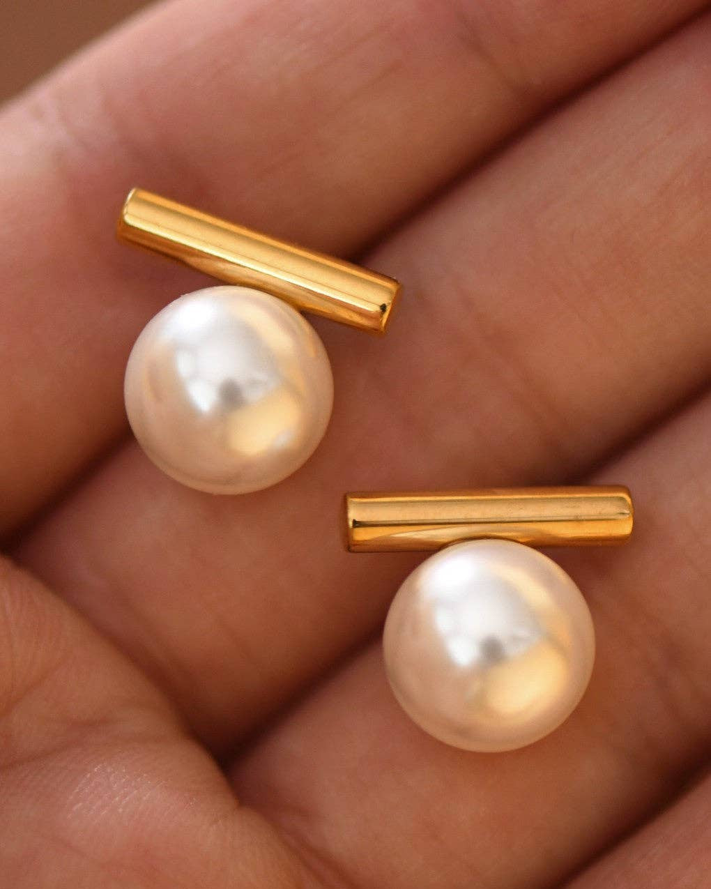 Pearl earrings with gold bars on a hand