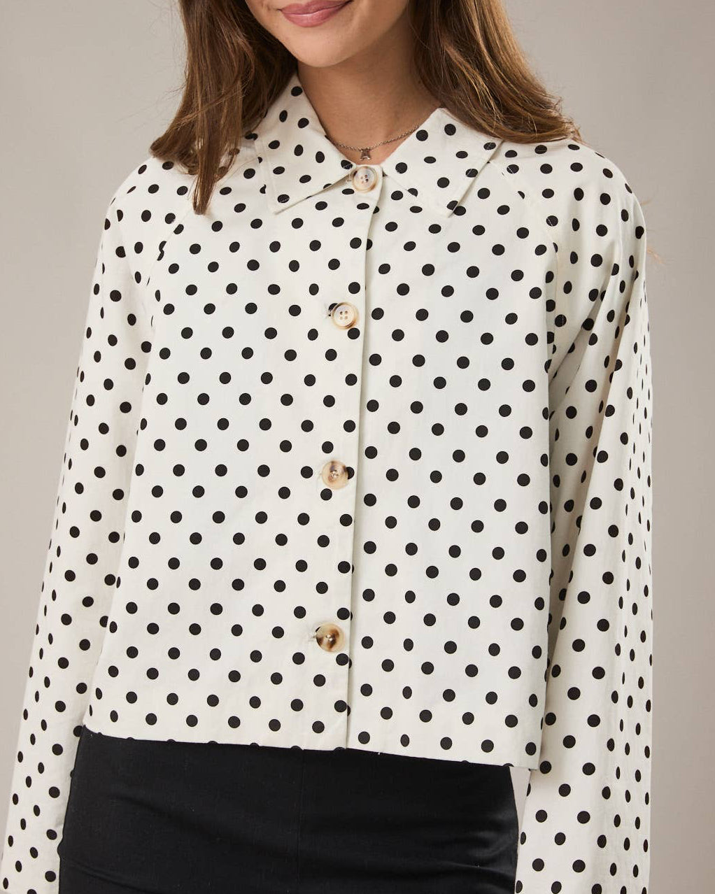 Woman wearing a white blouse with black polka dots and black pants on a neutral background