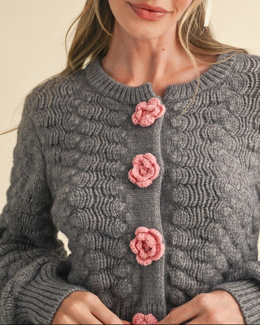 Woman wearing a gray knitted cardigan with pink floral buttons against a beige background
