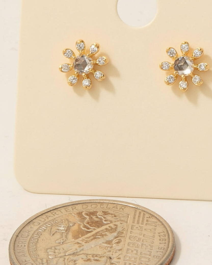 Gold earrings with cubic zirconia stones on a beige card, next to a coin for scale.