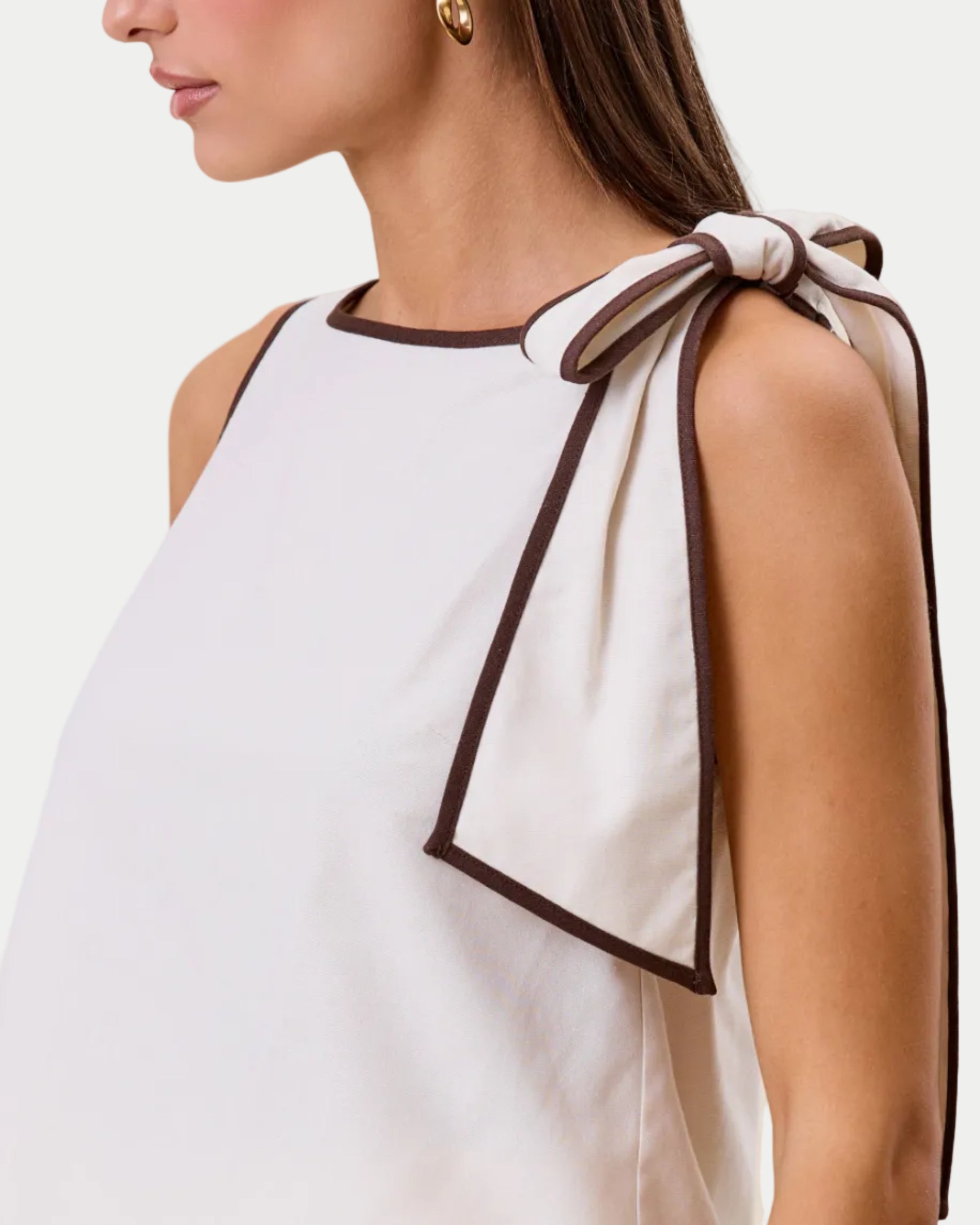 Woman wearing a white sleeveless top with a bow detail on a beige background