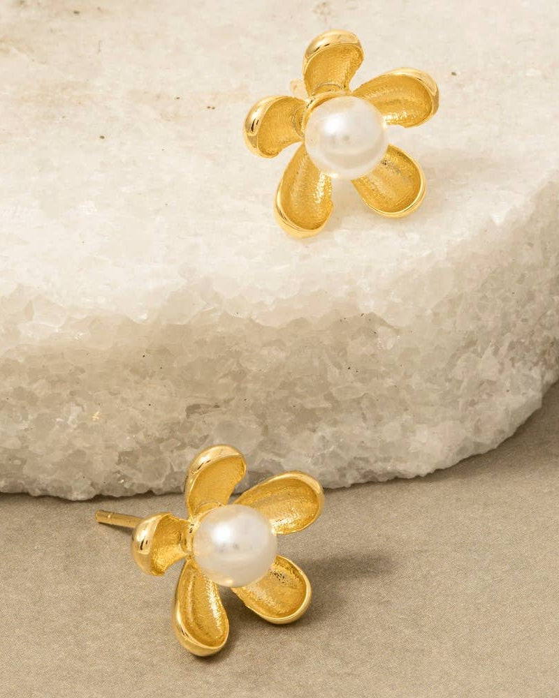 Gold flower-shaped earrings with pearl centers on a stone surface