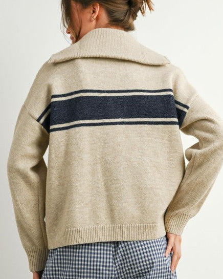Person wearing a beige sweater with a navy stripe on a plain background