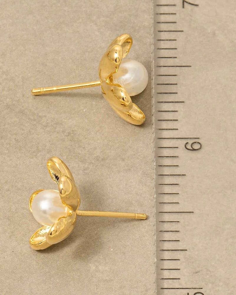 Gold earrings with pearls next to a ruler on a beige background