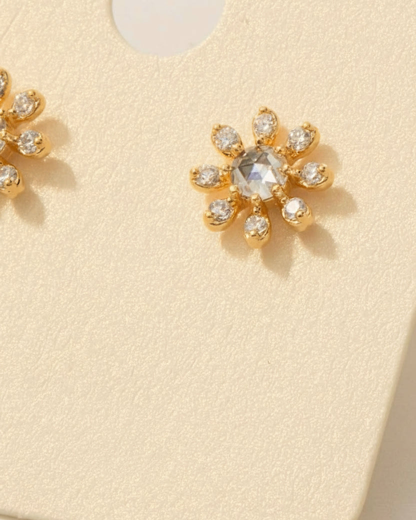 Gold earrings with zirconia stones on a beige card with text