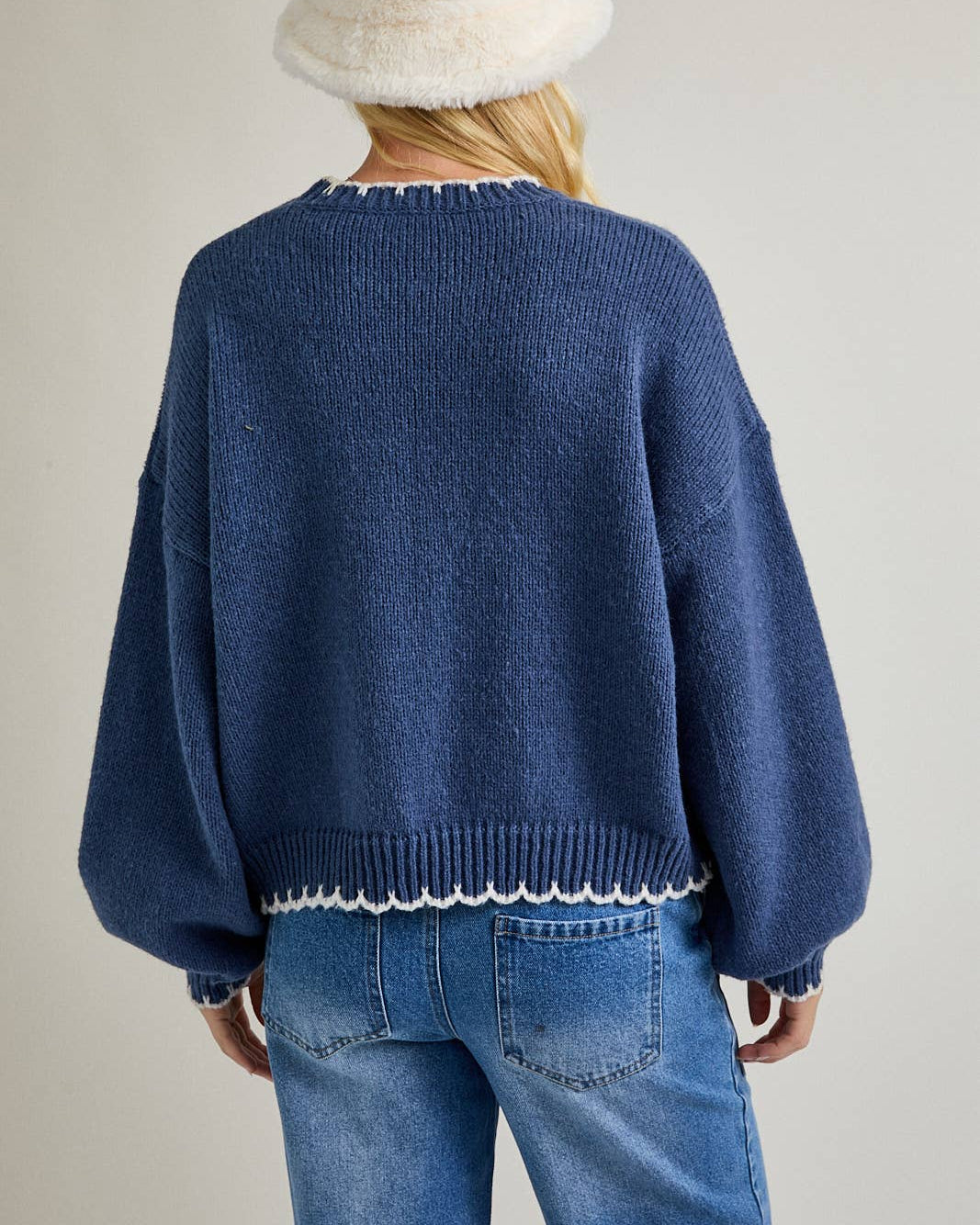 Person wearing a blue sweater with white trim and a white bucket hat on a plain background