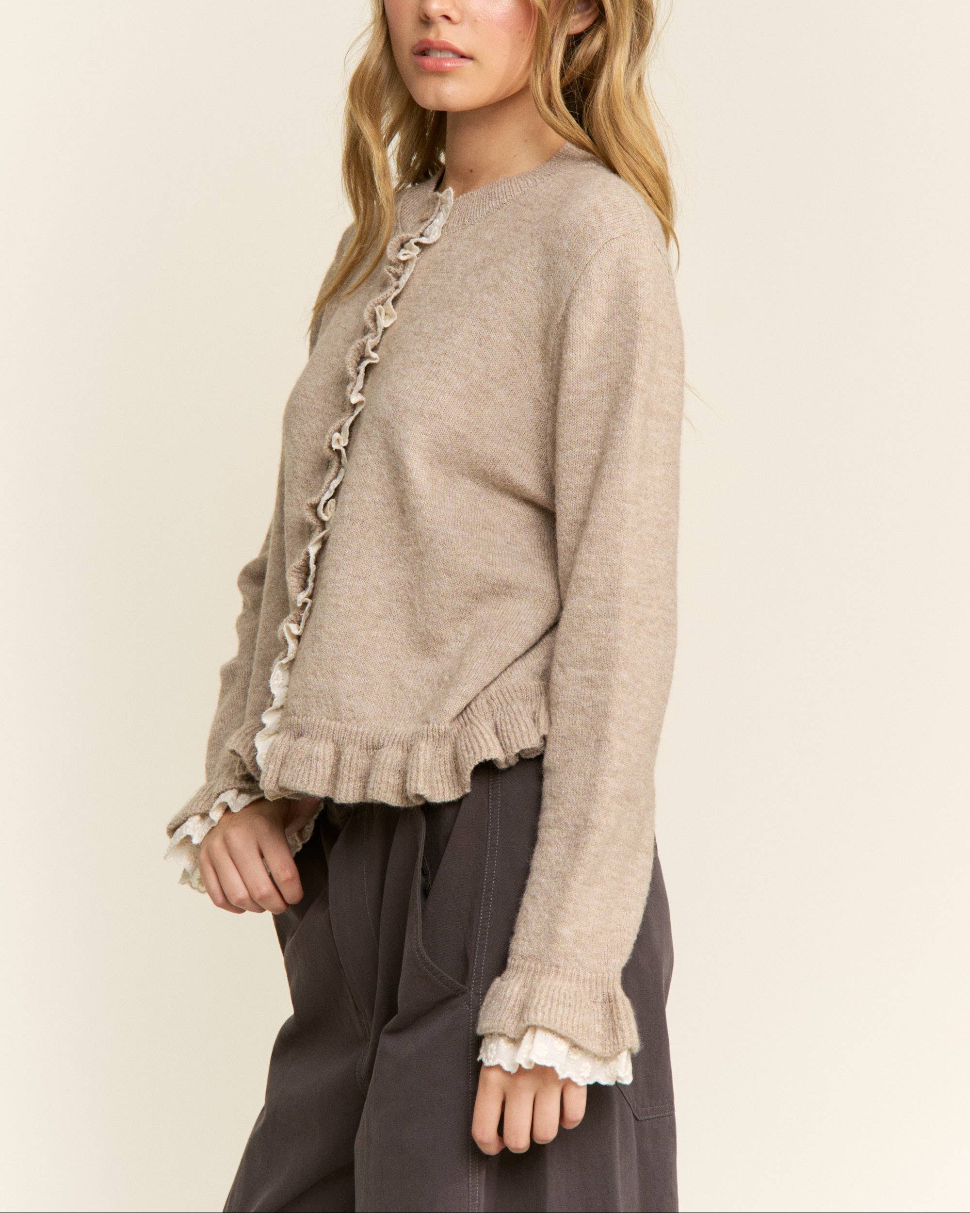 Woman wearing a beige sweater with lace trim on a plain background