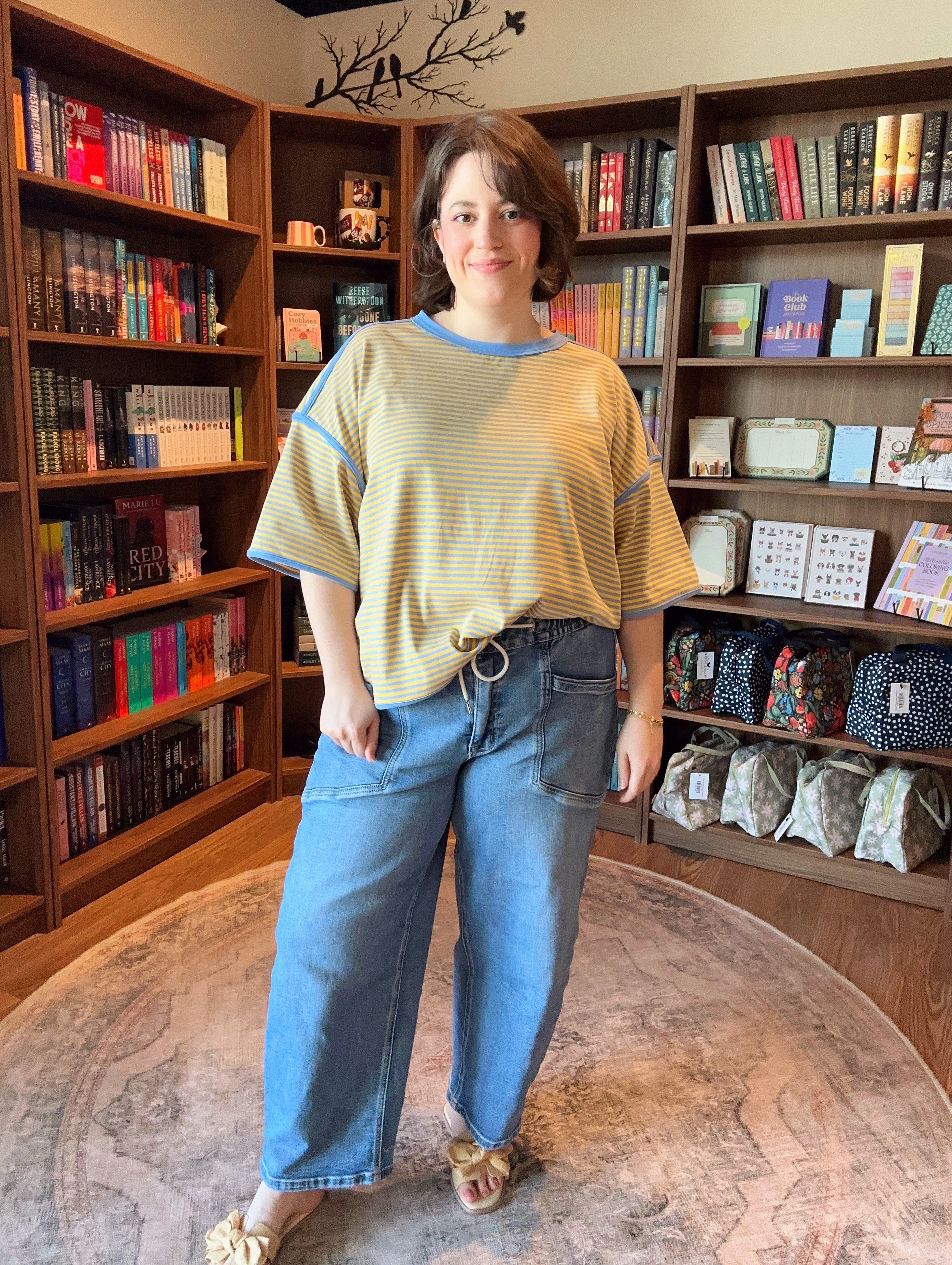 Woman standing in a room with bookshelves filled with books and decorative items.
