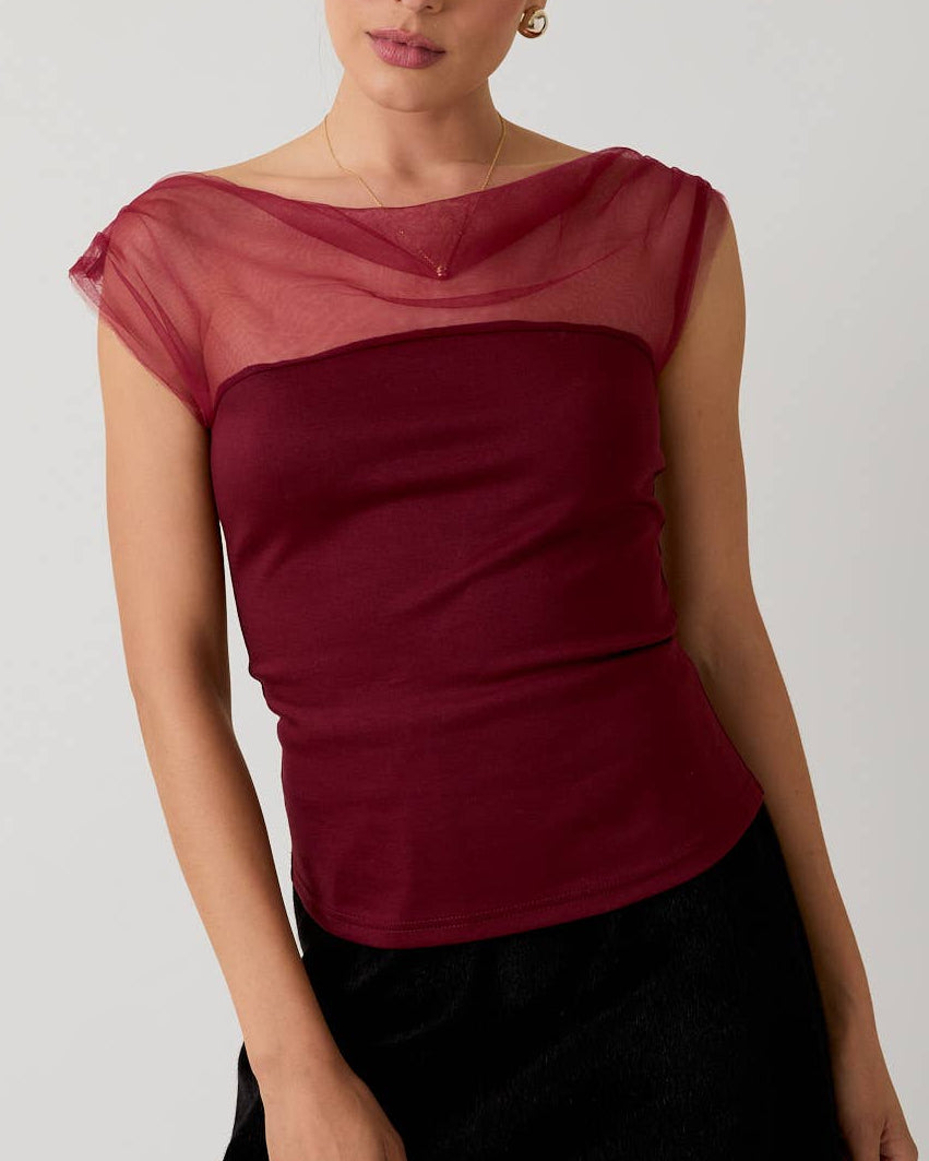 Woman wearing a red top with sheer sleeves and a black skirt on a white background