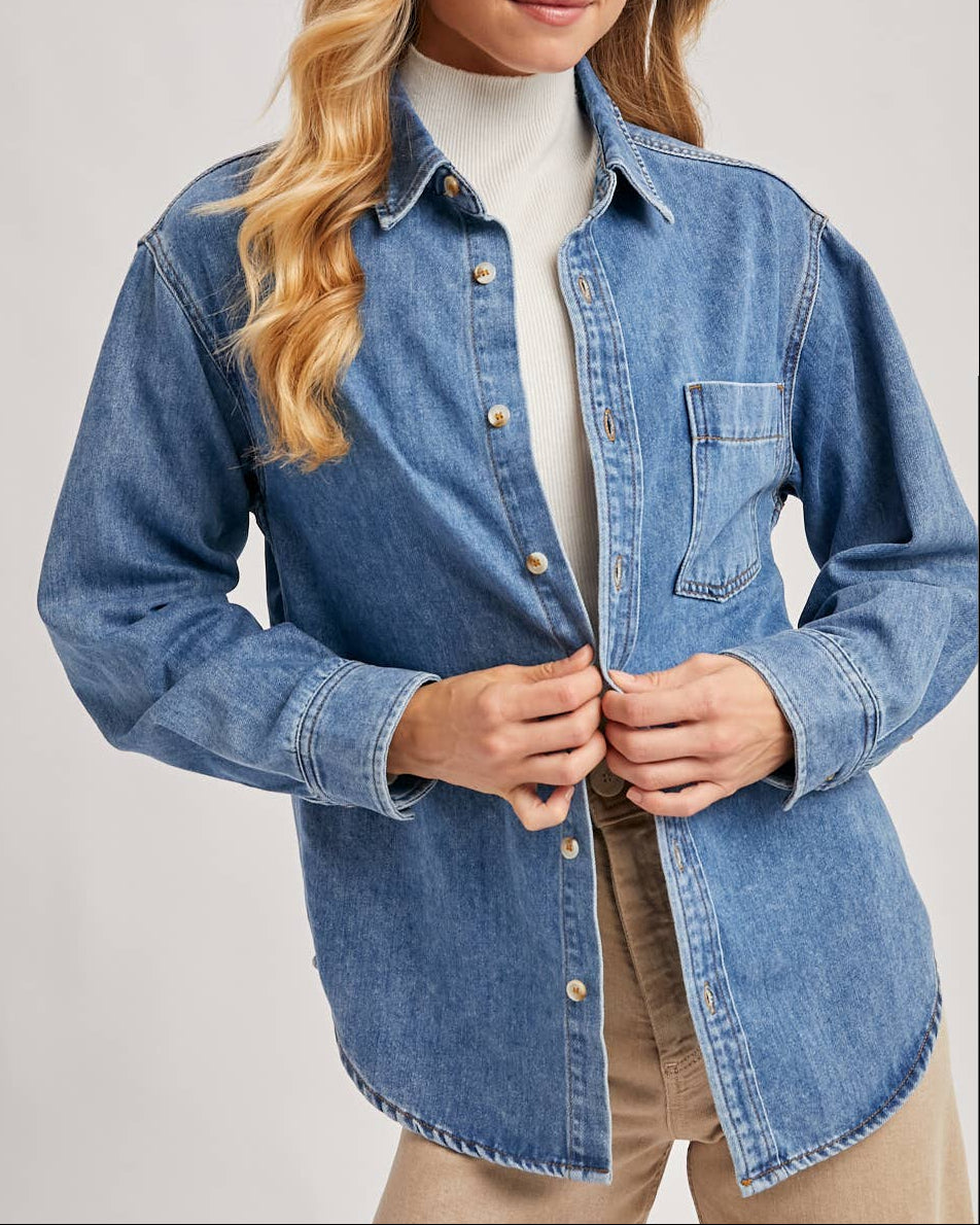 Woman wearing a blue denim shirt over a white turtleneck on a plain background