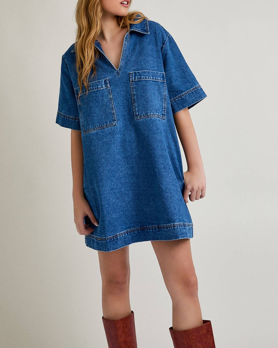 Woman wearing a blue denim dress and brown boots against a plain background