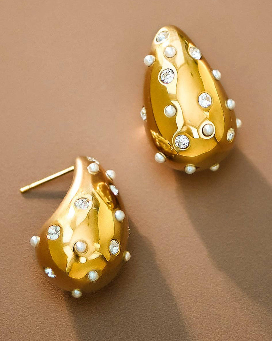 Gold teardrop earrings with pearl and gemstone accents on a brown background