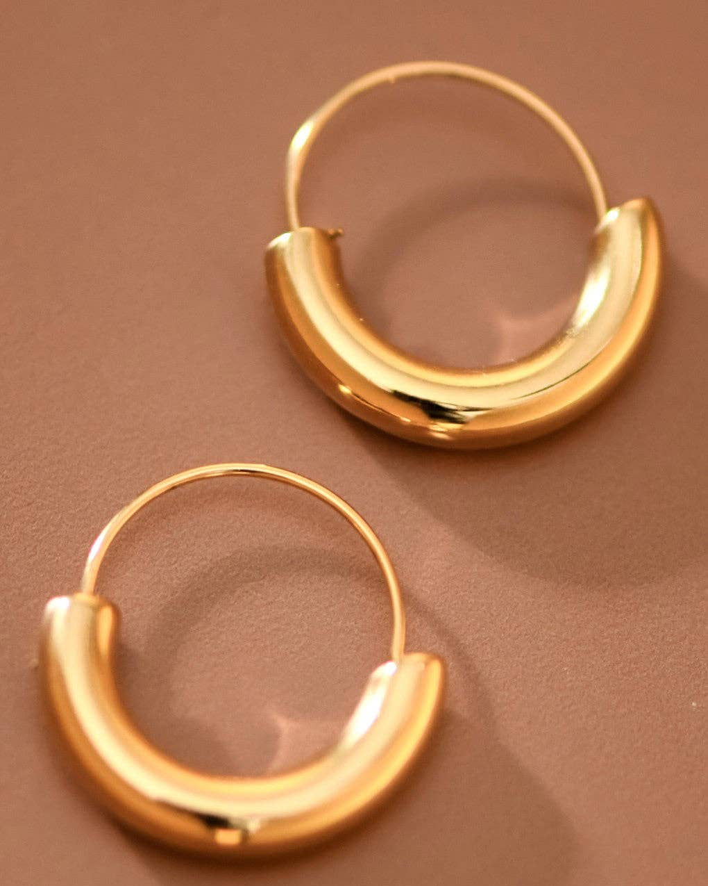 Gold hoop earrings on a brown background