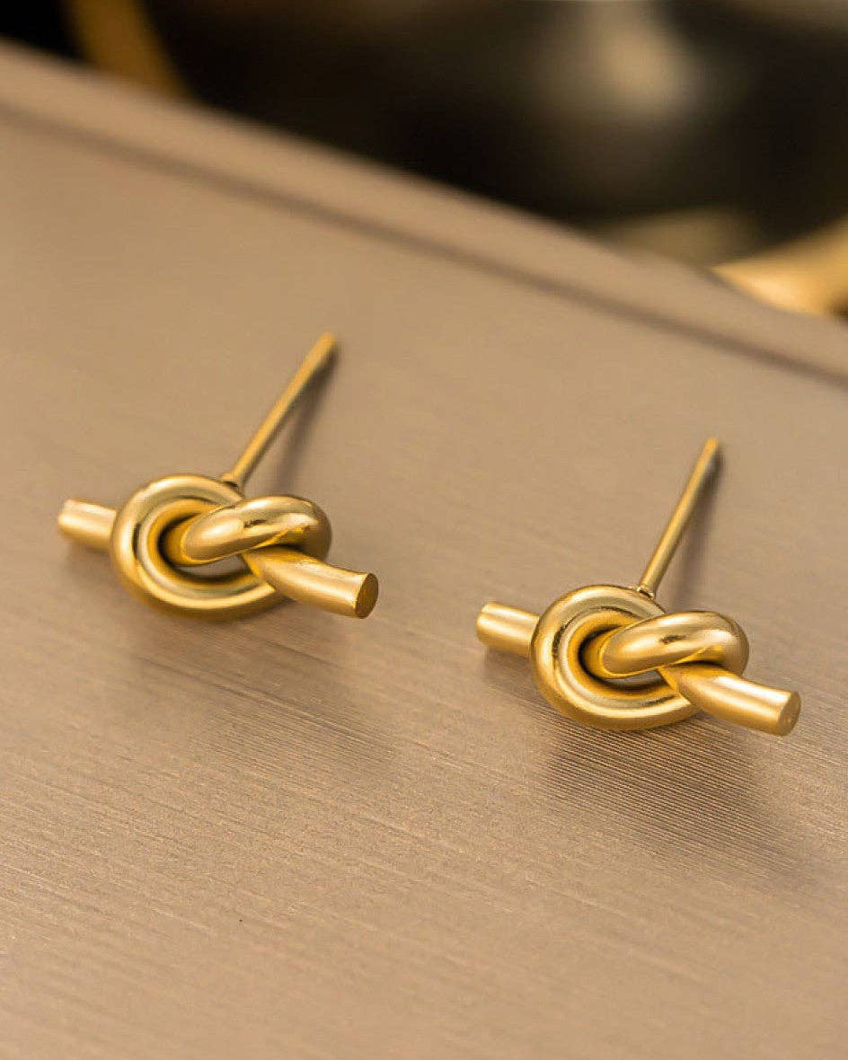 Gold knot-shaped earrings on a gold surface