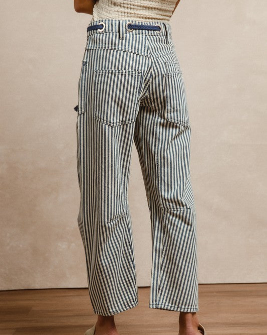 Person wearing striped pants on a wooden floor with a beige wall background