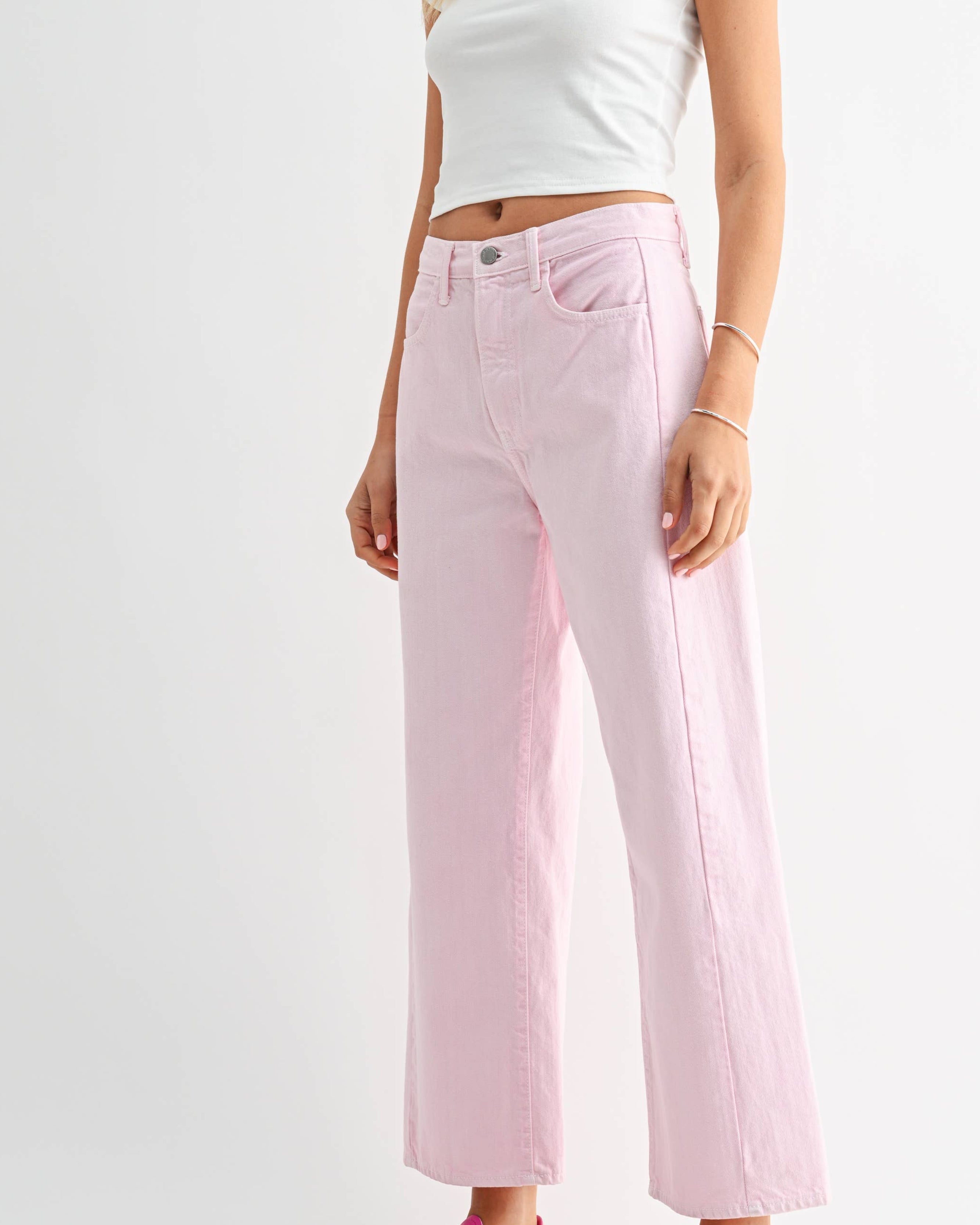 Woman wearing a white crop top and pink jeans on a white background