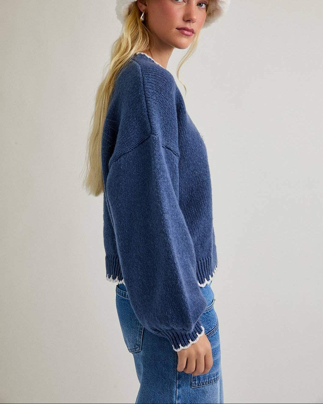 Woman wearing a blue sweater and white bucket hat on a plain background