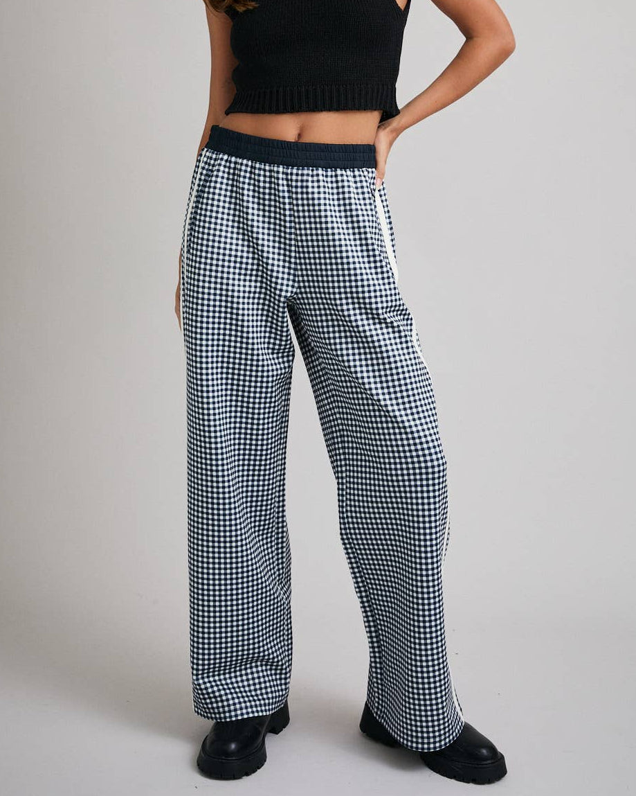 Woman wearing a black sleeveless top and checkered pants on a plain background