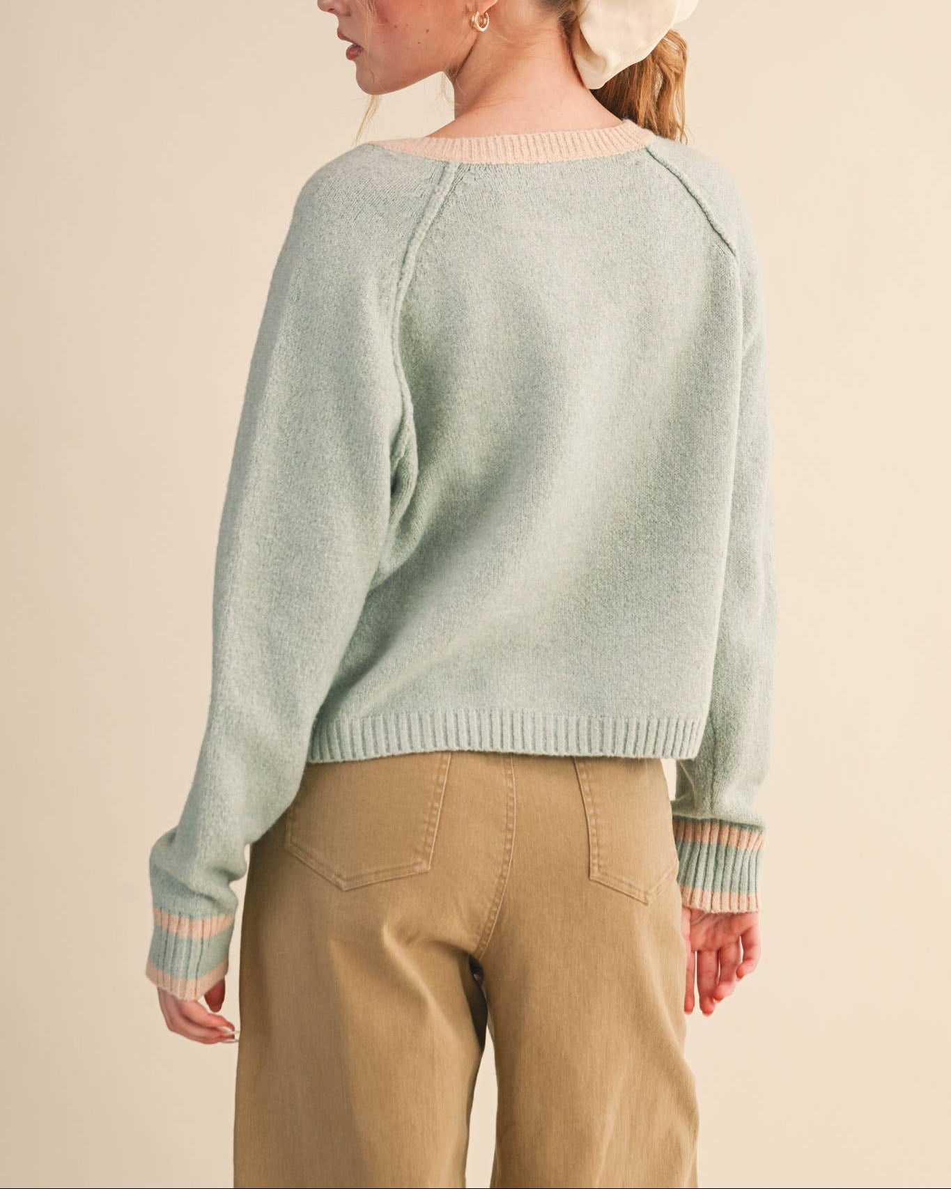Woman wearing a light green sweater and beige pants against a beige background