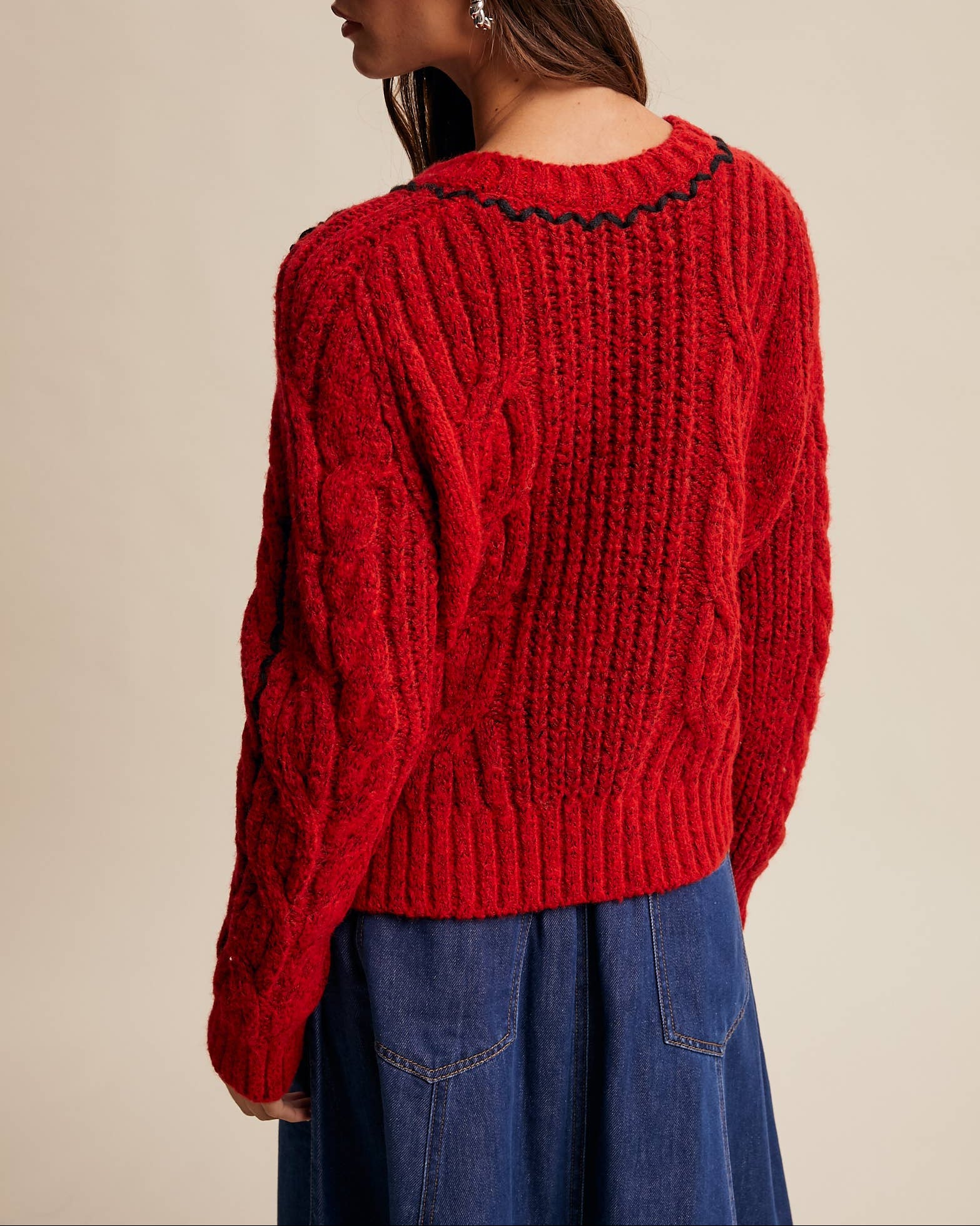 Person wearing a red knitted sweater and red cap on a beige background