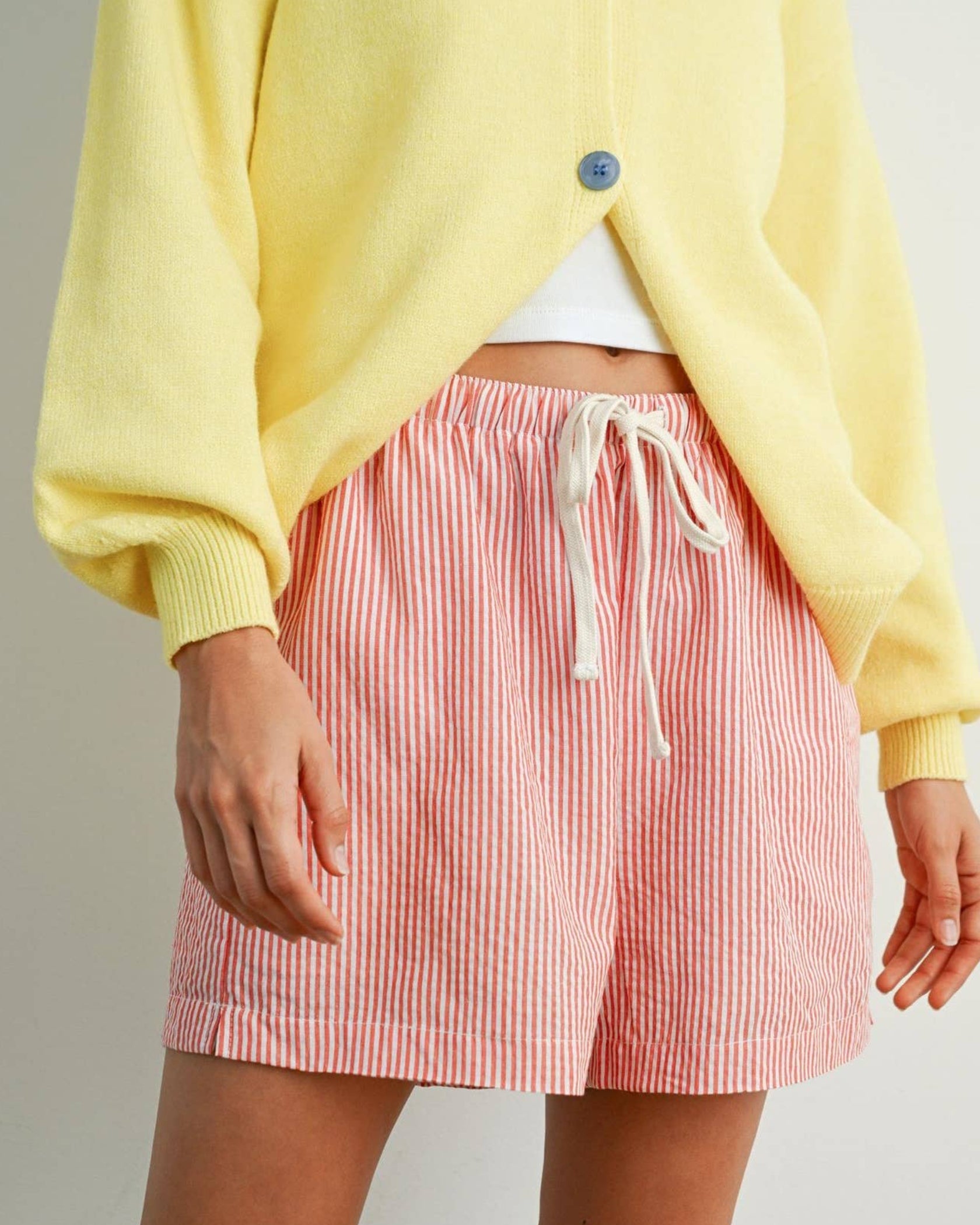 Person wearing a yellow cardigan and red and white striped shorts on a plain background