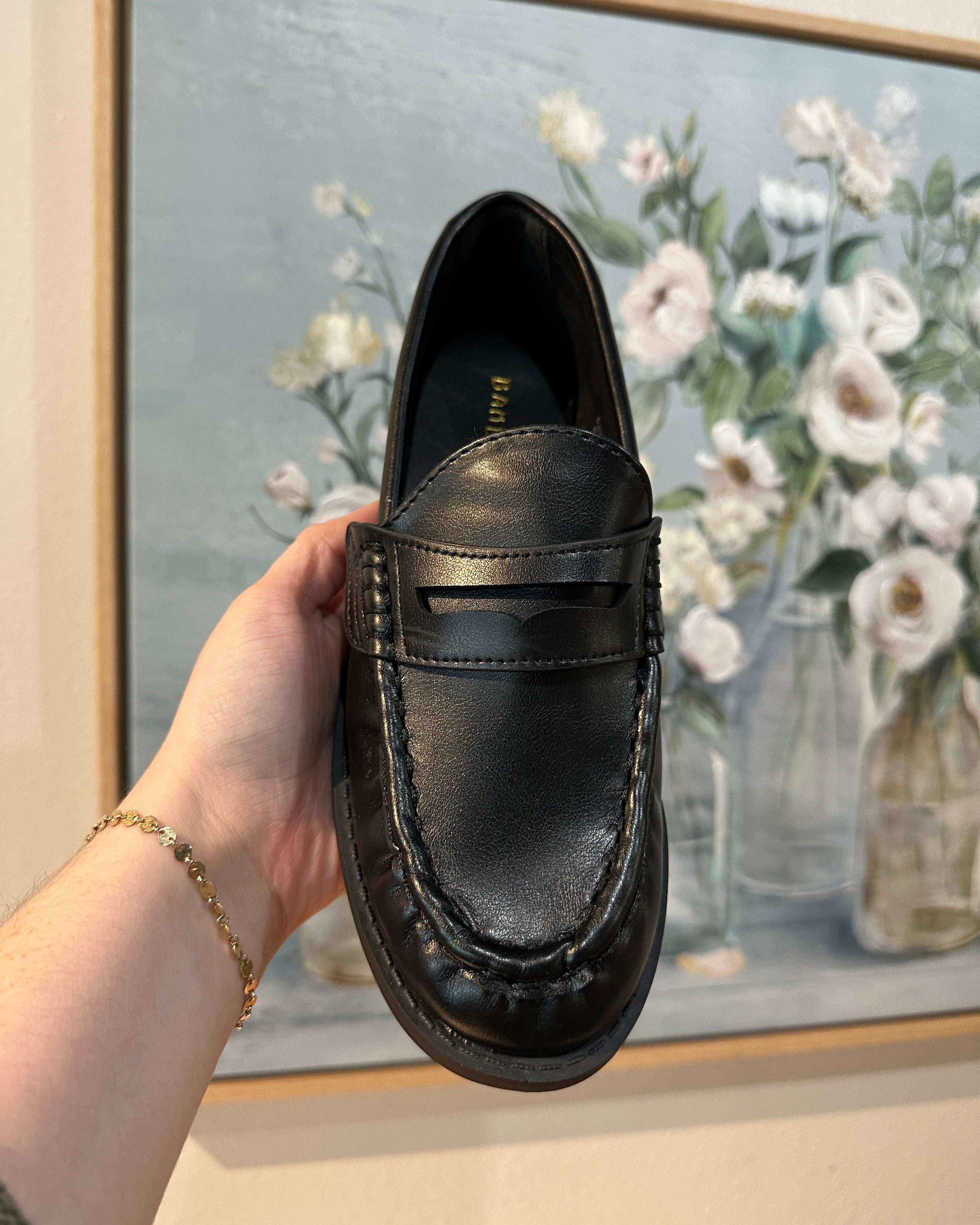 Black leather shoe held in front of a floral painting