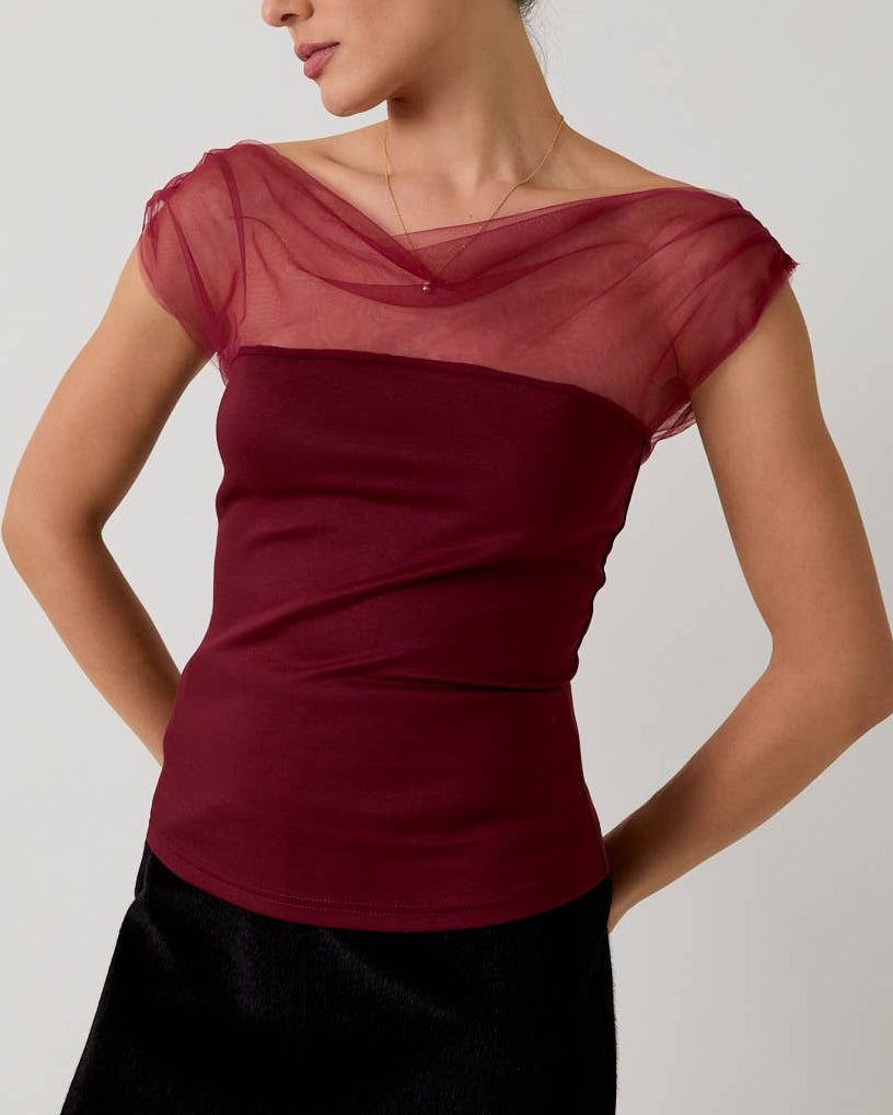 Woman wearing a burgundy top with sheer sleeves and a black skirt on a plain background