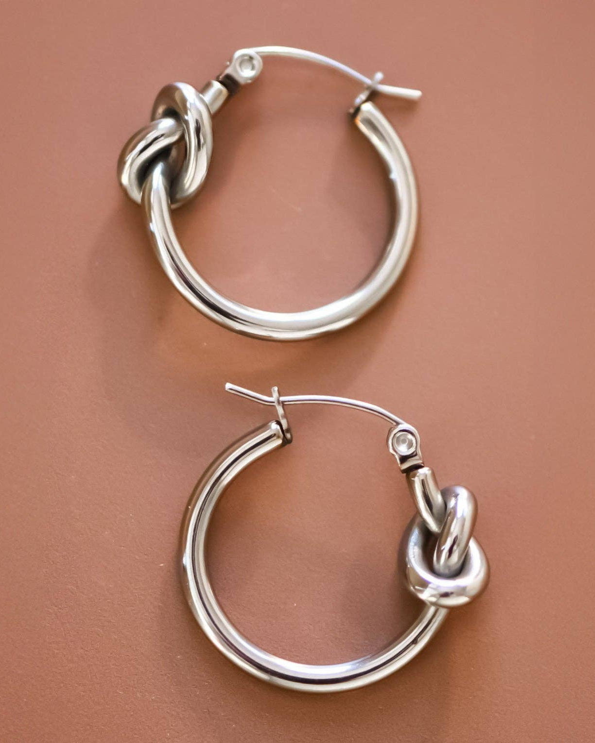Silver hoop earrings with knot design on a brown background
