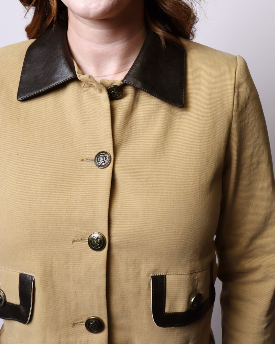 A close-up of a person wearing a tan jacket with a contrasting black collar and black button details.