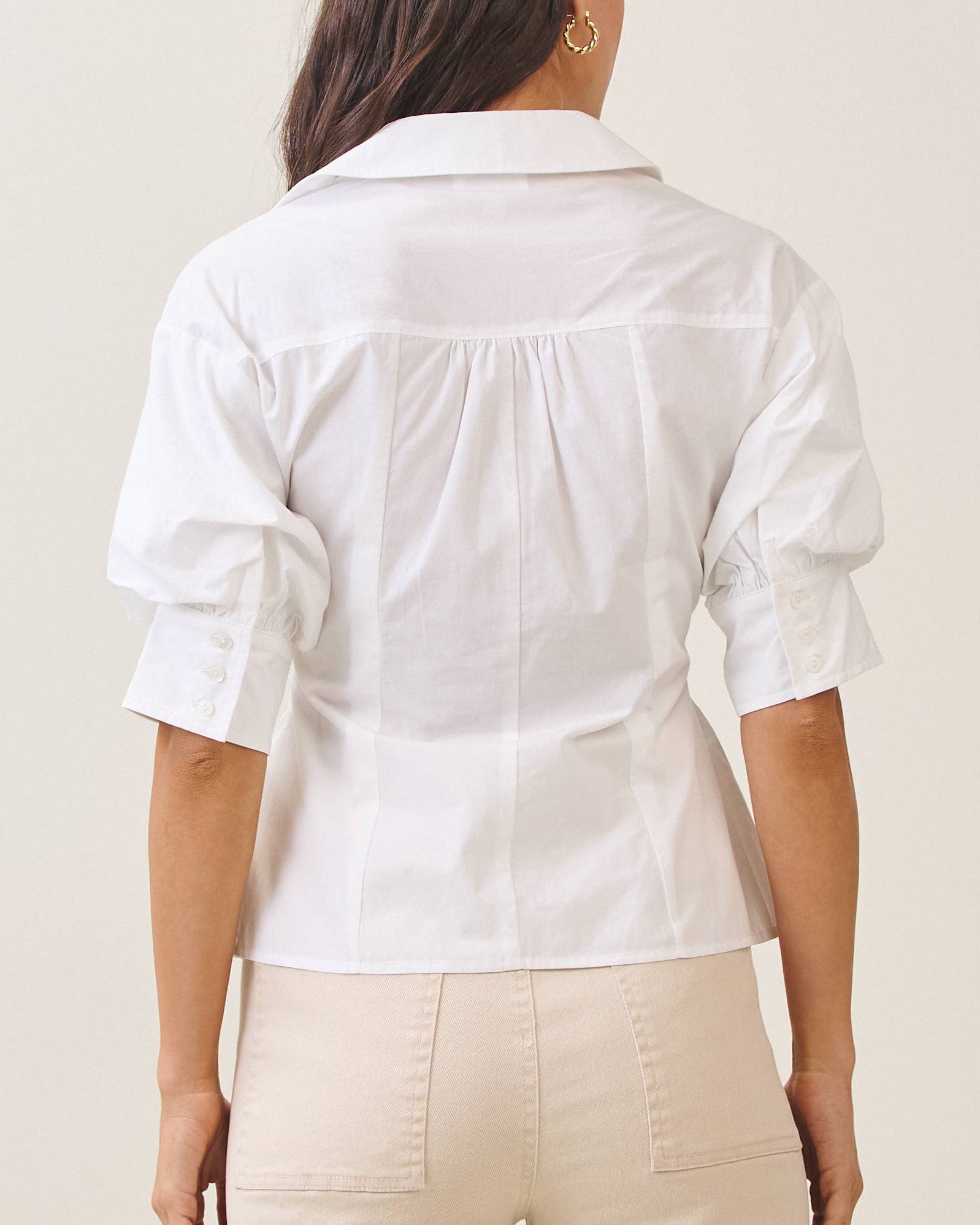 Model wearing a white blouse against a neutral background back view