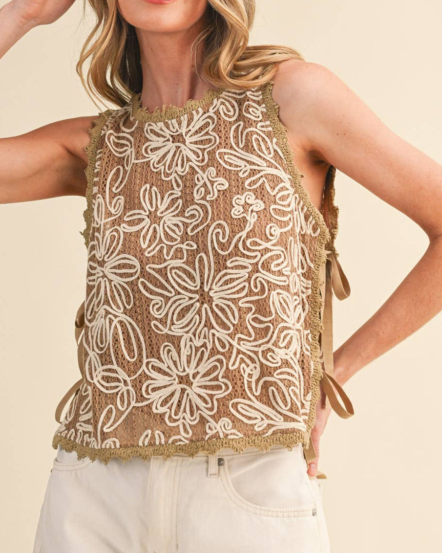 Woman wearing a beige sleeveless top with floral lace details and white shorts on a beige background