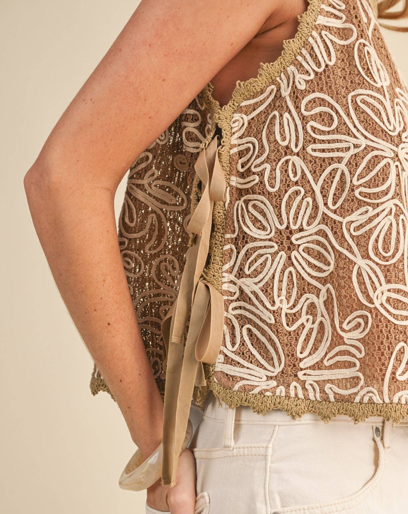 Close-up of a person wearing a beige lace top with a beige background