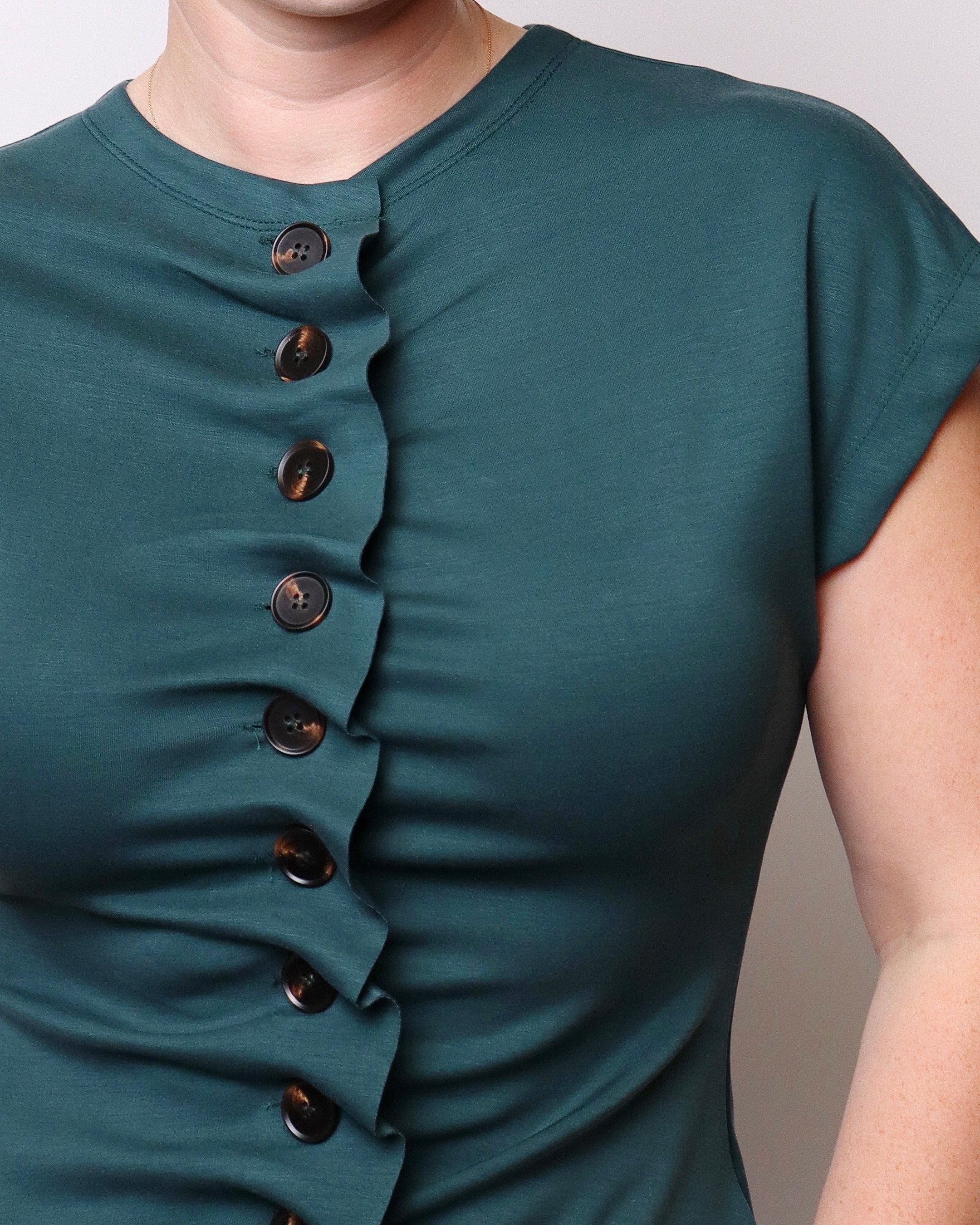 Close-up of a person wearing a short-sleeve teal top with a vertical row of dark buttons down the front.
