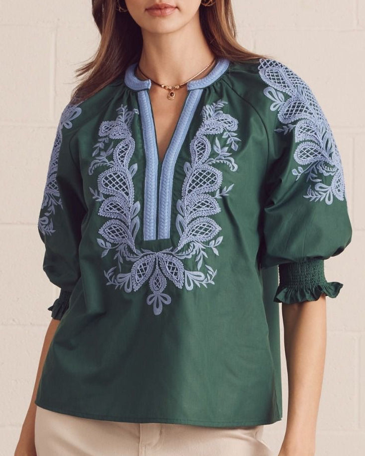Model wearing a green blouse with blue embroidery against a neutral background