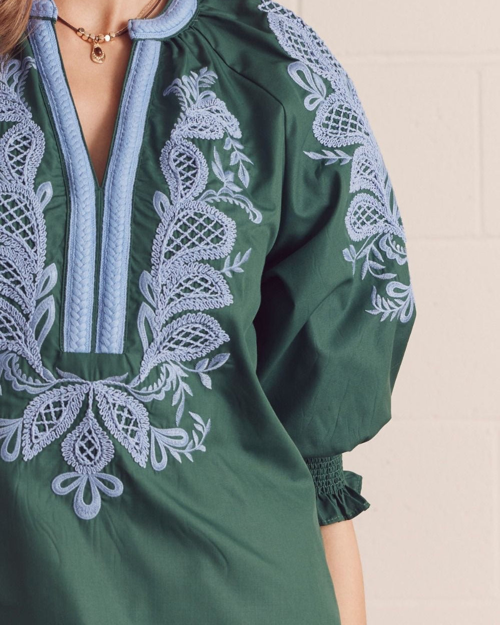 Model wearing a green blouse with blue embroidery against a neutral background close up