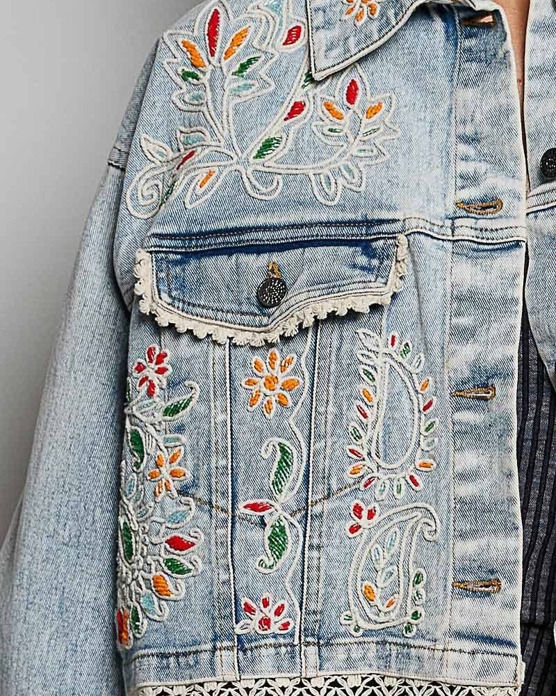 Model wearing a denim jacket with embroidery and beading.  Greens, oranges, and reds in the embroidery and beading.  Lace accents at the waist and cuff.