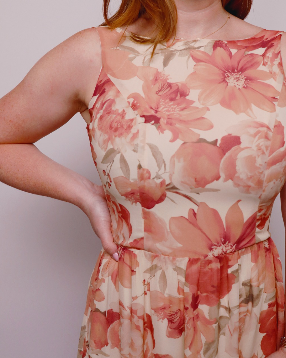 Person wearing a floral dress with pink and orange flowers on a plain background. Close up view