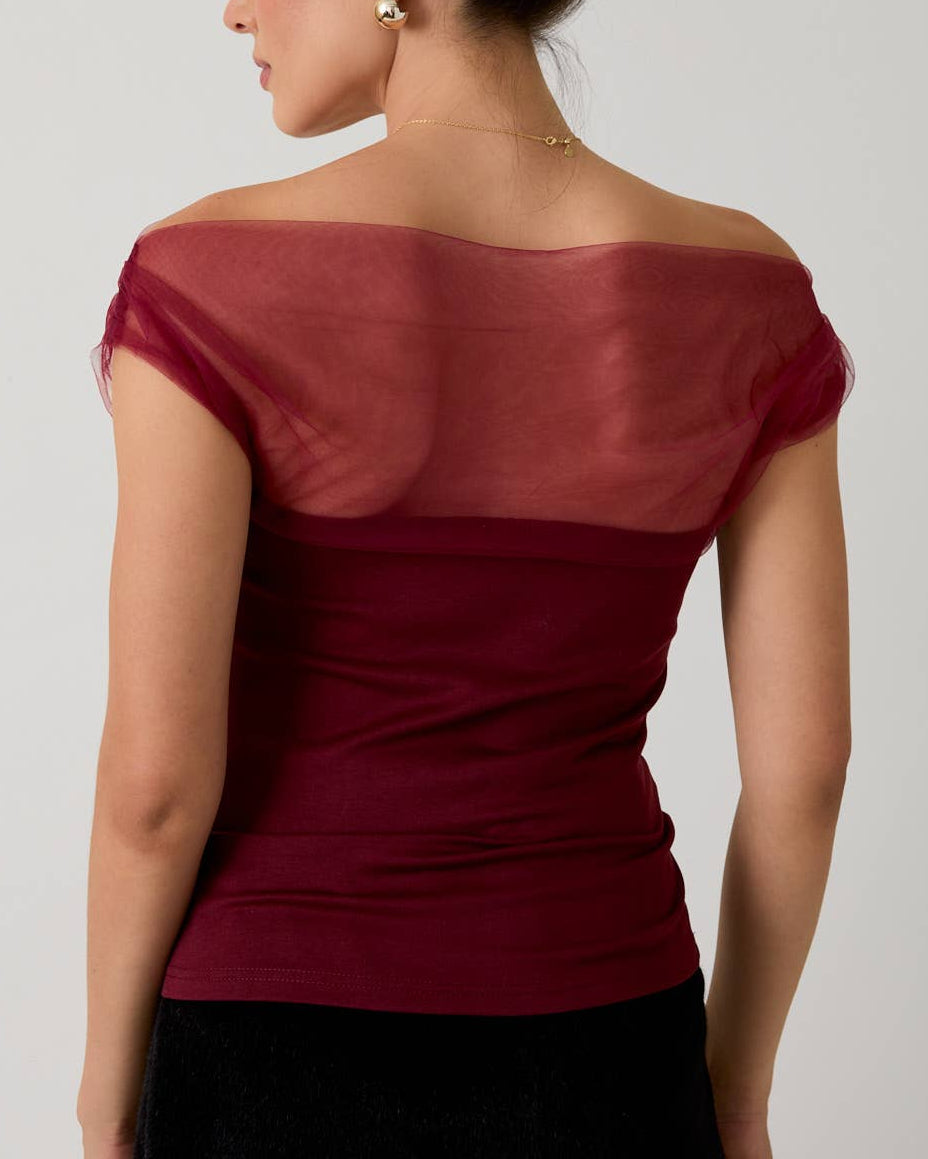 Woman wearing a burgundy off-shoulder top against a plain background