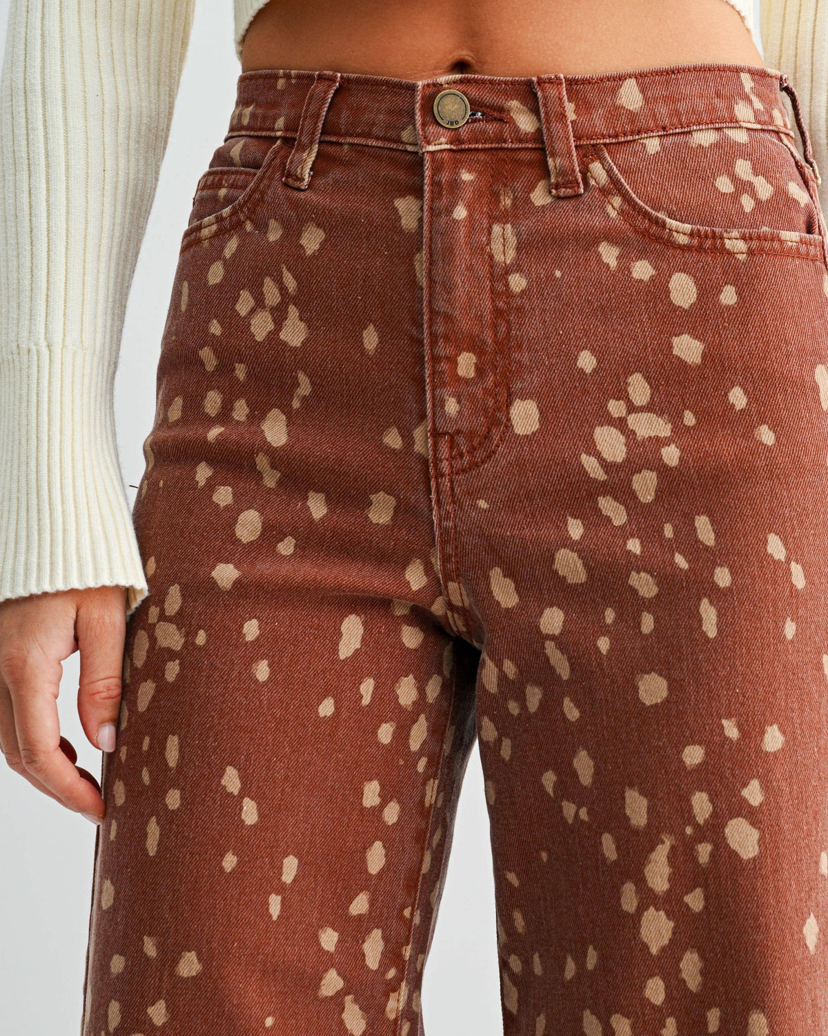 A close-up of a person wearing rust-brown wide-leg jeans with a beige speckled pattern, paired with a cream ribbed crop top against a light gray background. Bambi Deer Print Seamed Slim Wide Leg Jeans | Blackbird Boutique